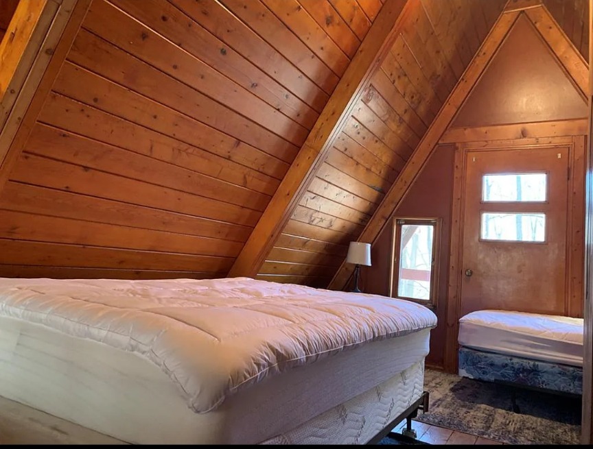 Loft before — bare mattress under exposed wood A-frame ceiling